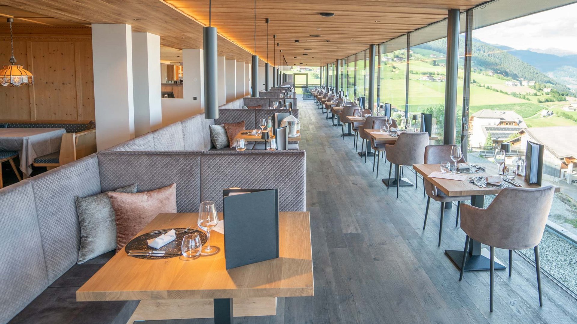 Panoramaspeisesaal im Hotel Purvita in Meransen mit großen Panoramafenstern, Holzdecke und schön gedeckten Tischen, Blick auf Dolomiten und Pustertal – ideal für Frühstück, Mittag- und Abendessen mit Panoramablick