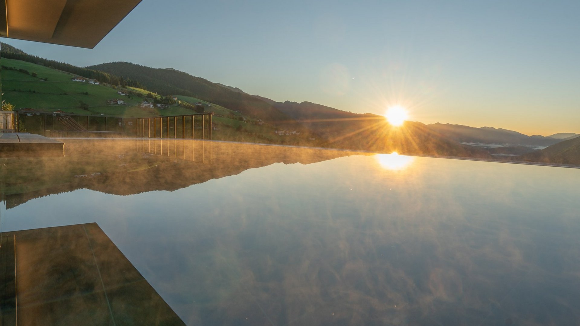 [Translate to Englisch:] Infinitypool im Hotel Purvita in Meransen bei Sonnenaufgang mit Panoramablick auf das Pustertal, die Dolomiten und die umliegende Berglandschaft Südtirols – ideal für Wellnessurlaub, Entspannung und Luxusurlaub in den Bergen