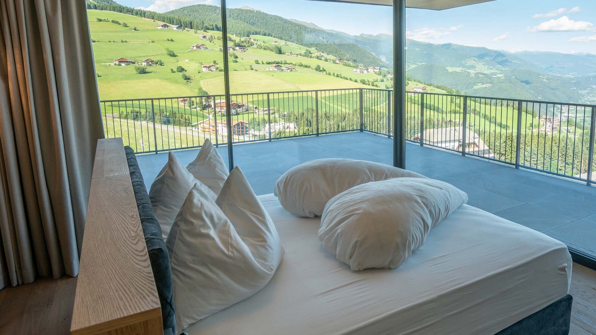 [Translate to Englisch:] Suite im Hotel Purvita in Meransen mit großem Bett, Hängelampe, Eckfenstern und Balkon, Panoramablick über Meransen, Gitschberg, Pustertal und die Dolomiten, ideal für Luxusurlaub, Bergblick und entspannte Ferien in Südtirol